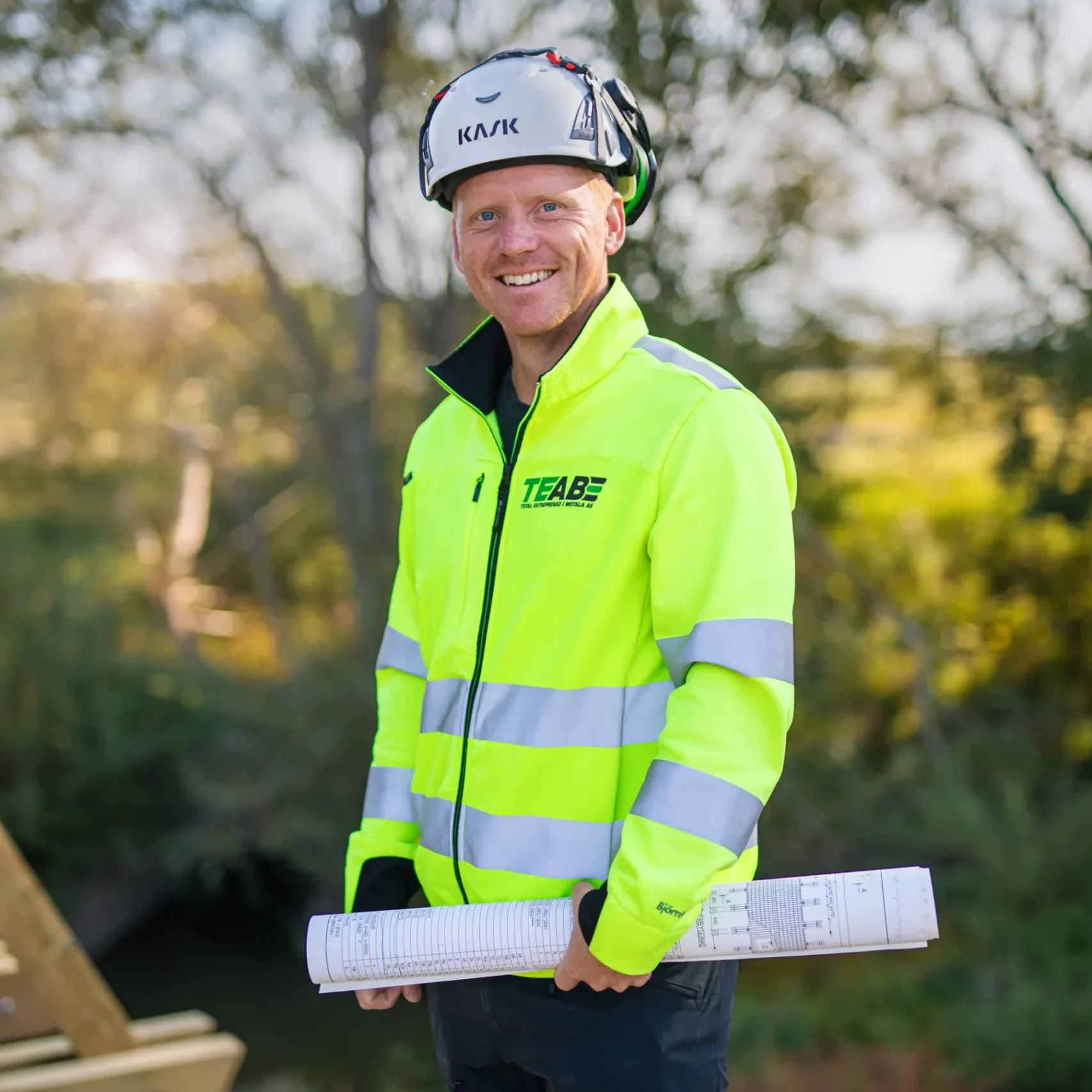 TEAB-tjänsteman i varselkläder och hjälm håller ritningar på en byggarbetsplats utomhus.